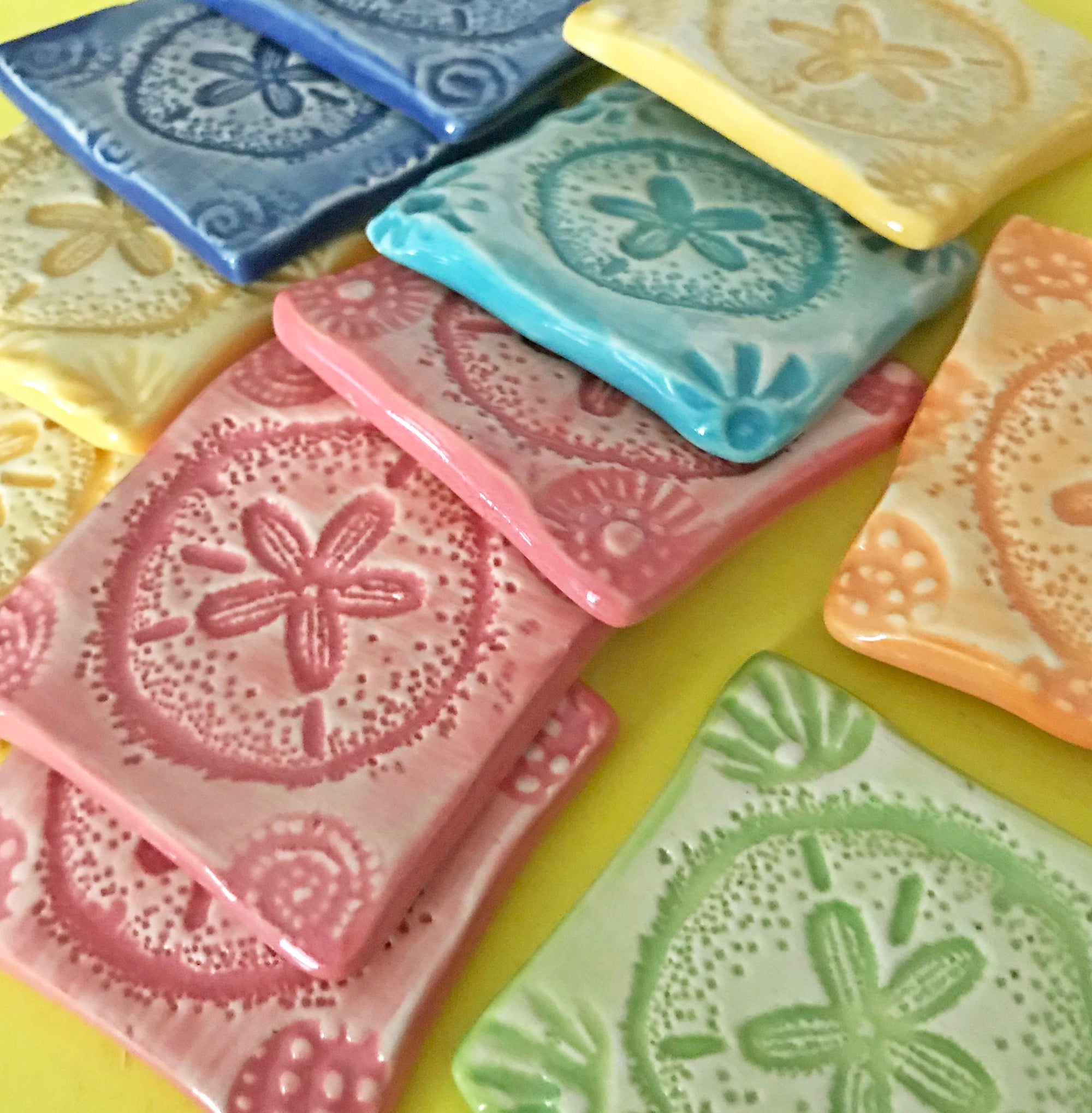 The pattern, drawn by Lorraine Oerth, is pressed into soft clay.  Once dry, it is glazed in happy bright colors. 